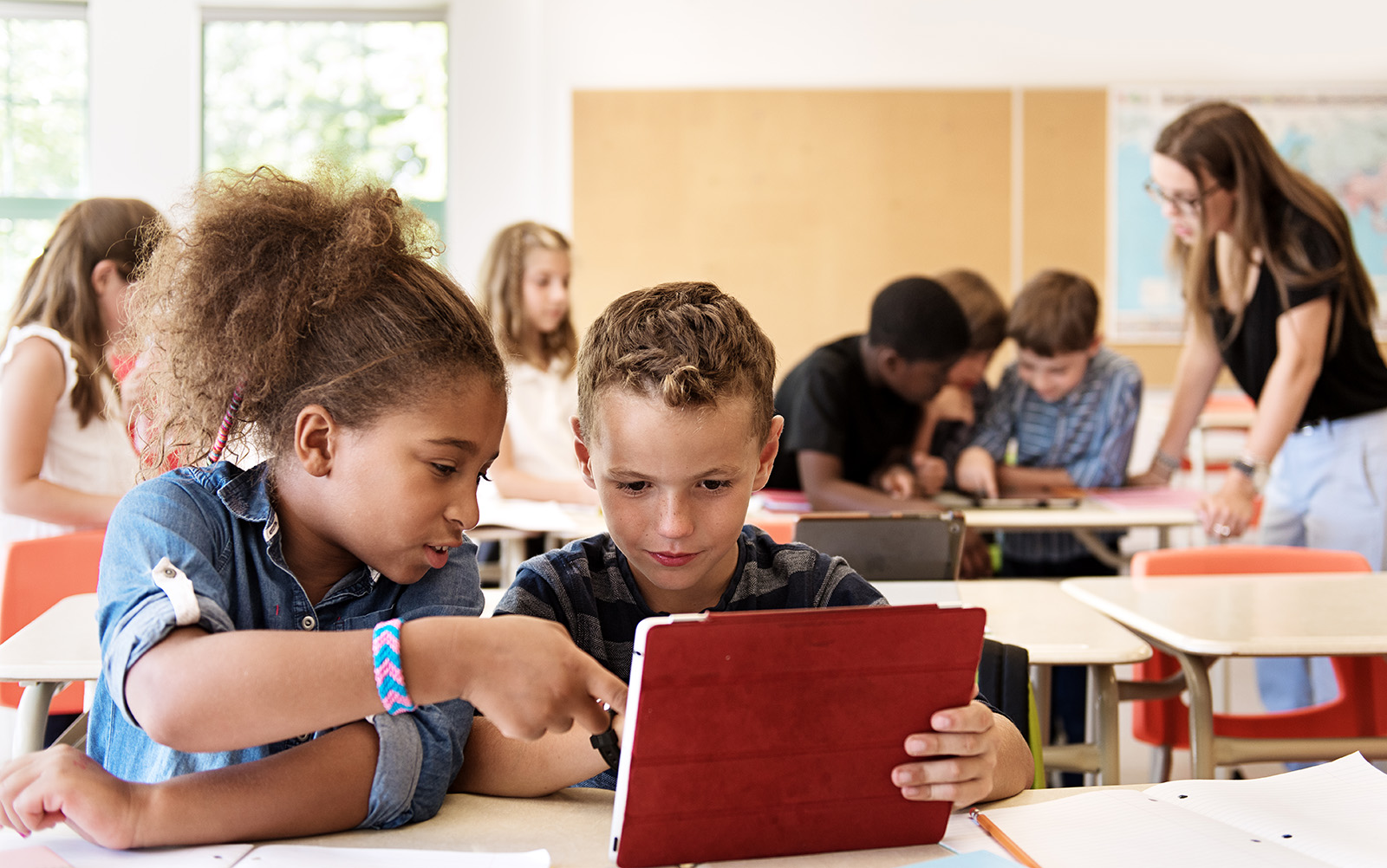 Two elementary students work together with an iPad in a classroom.